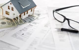 House, money, tax forms, and glasses on table